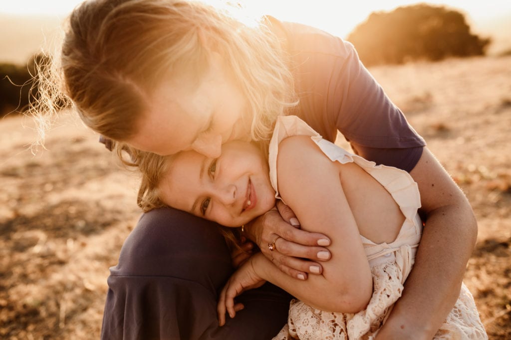 Mother and daughter snuggling during golden hour photography session in Knowland Park, Oakland