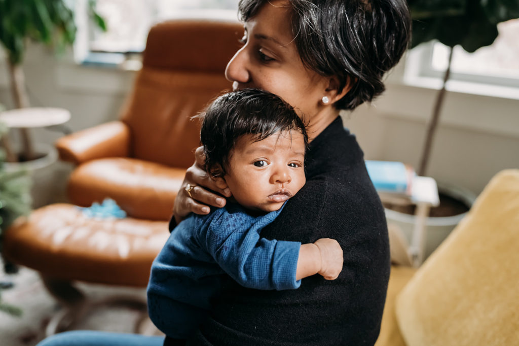 Sweet mother and newborn son sitting together in their Oakland, CA living room during their newborn documentary photography session with Xilo Photography