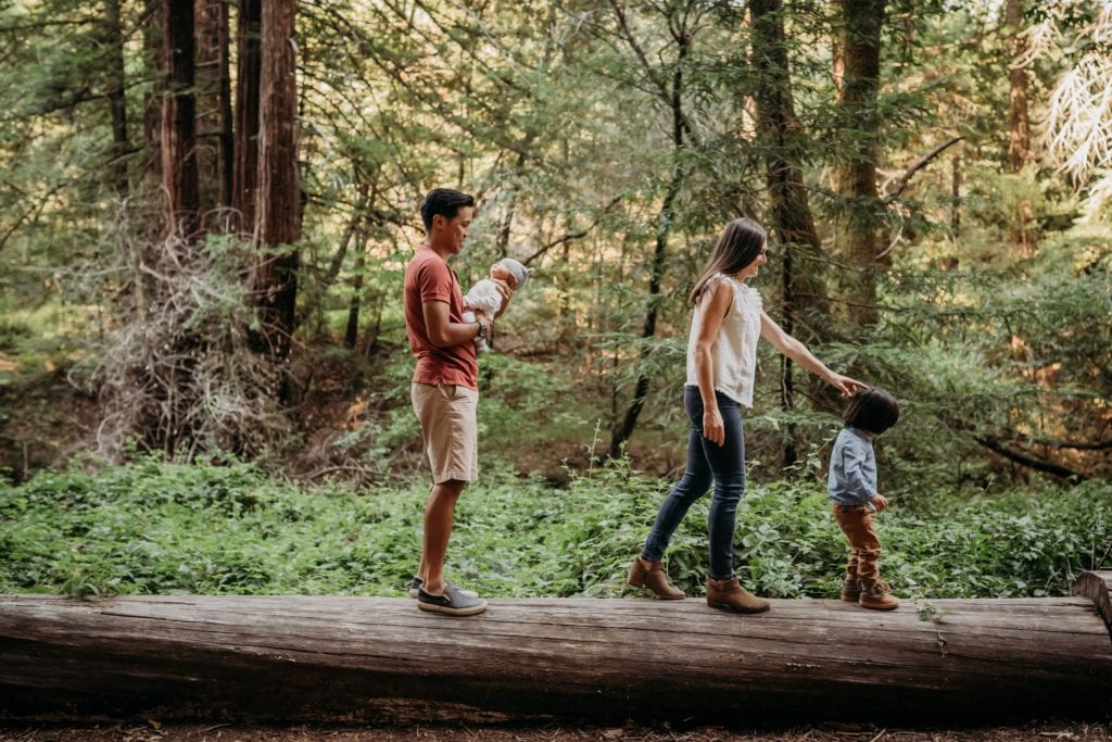 Family of 4 walking across log during family photography session with Xilo Photography at Redwood Regional Park in Oakland, CA.