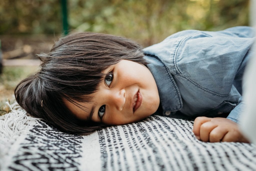 Child lays on striped blanket smiling at camera during family photography session with Xilo Photography at Redwood Regional Park in Oakland, CA.
