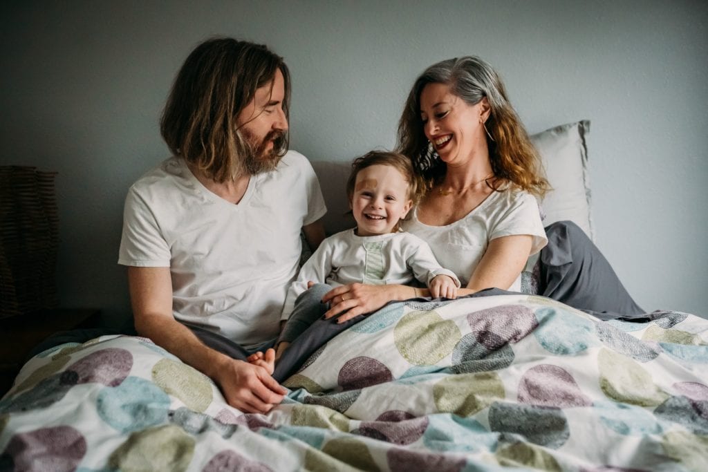 Family of three snuggles in bed during family photography session with Xilo Photography