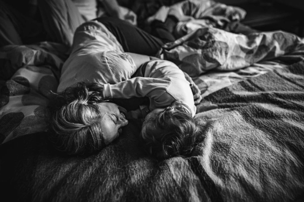Mama and toddler snuggle in bed during family photography session with Xilo Photography