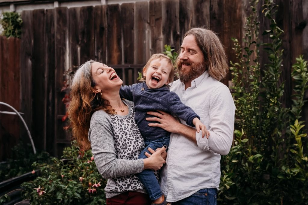 Family of three laughs together and gets silly in the backyard during family photography session with Xilo Photography