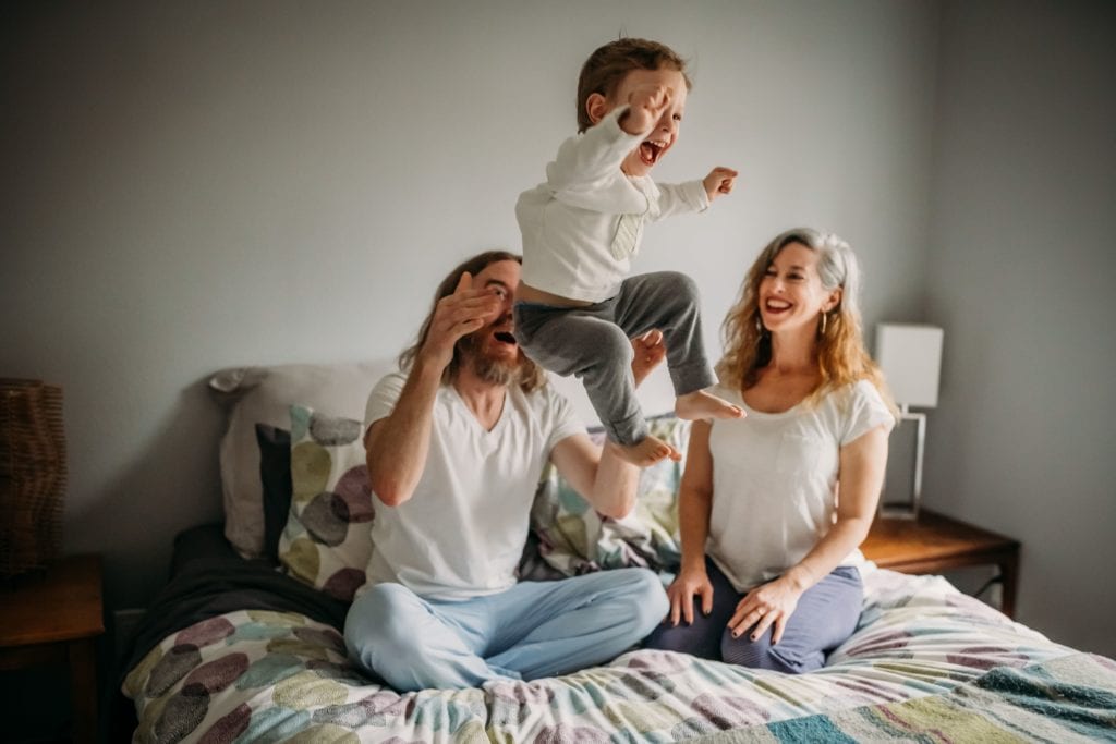 Family of three snuggles in bed during family photography session with Xilo Photography