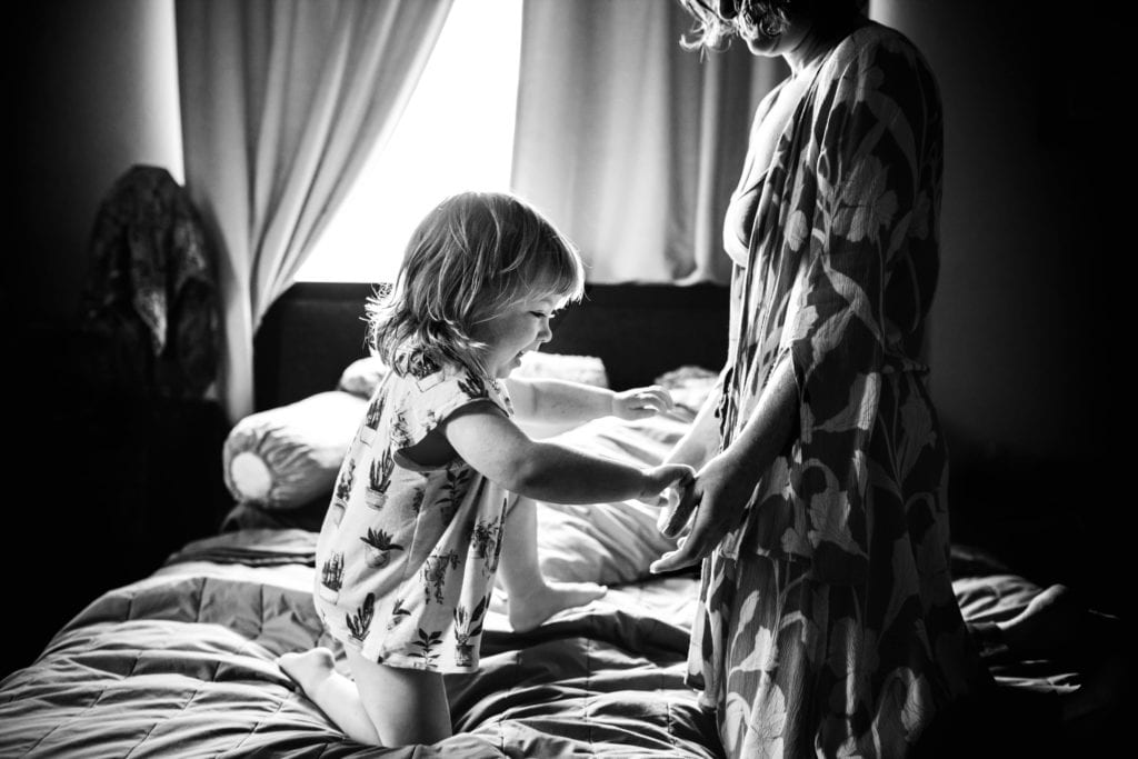 Mama and child play together on bed during a Motherhood Session with Xilo Photography