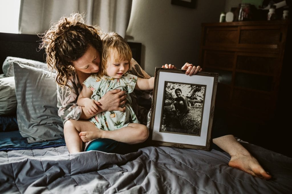 Mama and toddler hold framed picture of woman in bed during a Motherhood Session with Xilo Photography