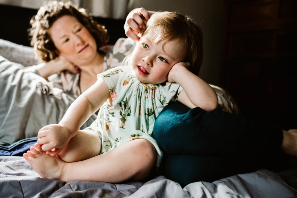 ama and toddler get cozy together on bed during a Motherhood Session with Xilo Photography