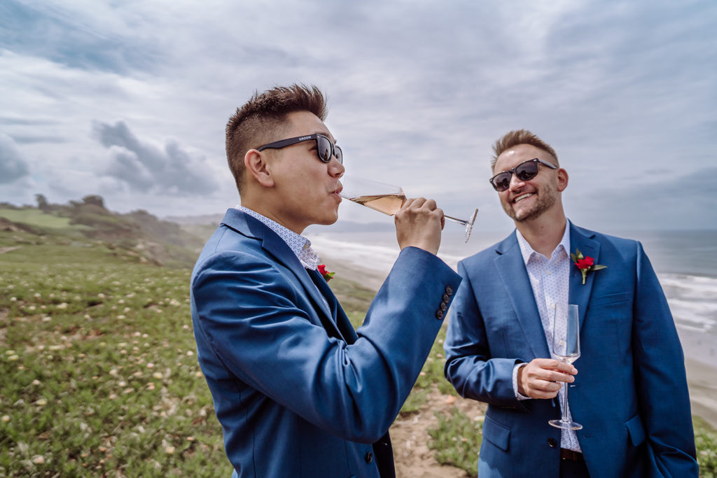 An inclusive and intimate wedding and elopement photographer, Xilo Photography, Kati Douglas who is based in Oakland, California in the bay area, took this picture of a same sex gay couple on their wedding day/elopement day as the two grooms pour themselves champagne so they celebrate their wedding day in their tuxes at Fort Funston, CA which was their intimate wedding venue. Ever wondered what is an intimate wedding or what would be considered a small wedding? This is a great example of both! 