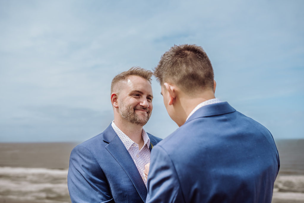 An inclusive and intimate wedding and elopement photographer, Xilo Photography, Kati Douglas who is based in Oakland, California in the bay area, took this picture of a same sex gay couple on their wedding elopement day as the two grooms look into eachother's eyes as they celebrate their wedding day in their tuxes at Fort Funston, CA which was their intimate wedding venue. Ever wondered what is an intimate wedding or what would be considered a small wedding? This is a great example of both! 