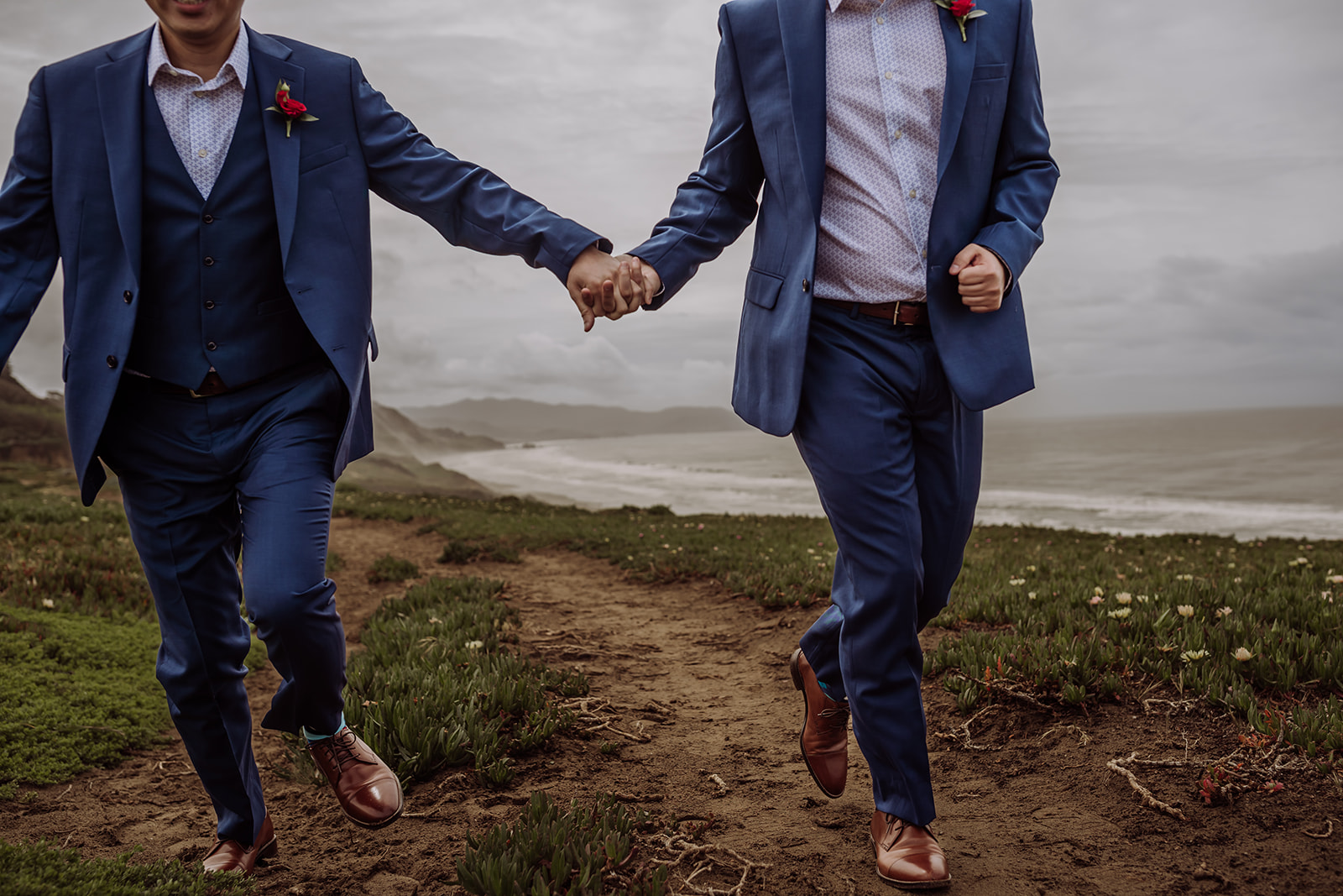 An inclusive intimate wedding and elopement photographer, Xilo Photography, Kati Douglas who is based in Oakland, California in the bay area, took this picture of a same sex gay couple on their wedding day/elopement day as the two grooms lean in near the beach with waves crashing in the background at Fort Funston, CA which was their intimate wedding venue. Ever wondered what is an intimate wedding or what would be considered a small wedding? This is a great example of both!