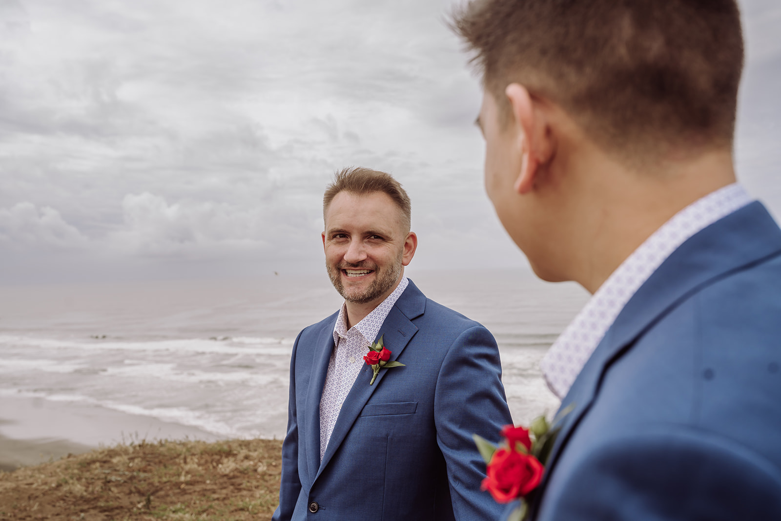 An inclusive intimate wedding and elopement photographer, Xilo Photography, Kati Douglas who is based in Oakland, California in the bay area, took this picture of a same sex gay couple on their wedding day/elopement day as the two grooms lean in near the beach with waves crashing in the background at Fort Funston, CA which was their intimate wedding venue. Ever wondered what is an intimate wedding or what would be considered a small wedding? This is a great example of both! 
