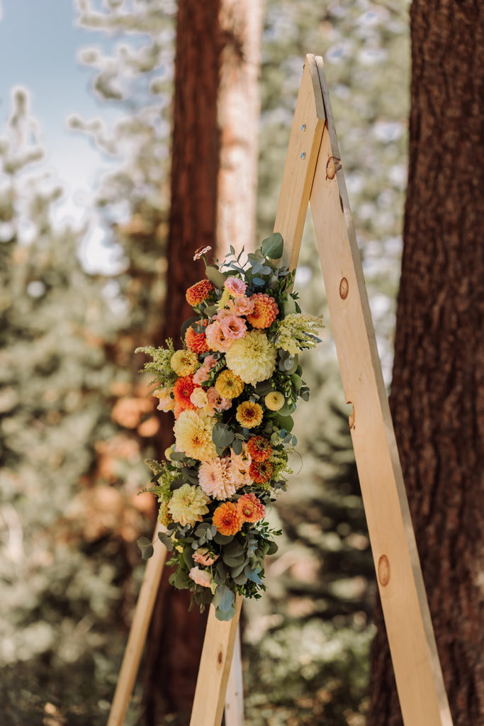 Pictured here is the wooden wedding decor mountain arch with floral wedding designs for inspiration for wedding planning. This was taken in Lake Tahoe, California during a mountain, forest wedding and beach wedding venue. This featured natural wood decor, and an outdoor forest beach ceremony. Photographed by Bay Area photographer, Kati Douglas with Xilo Photography based in Oakland, CA. 