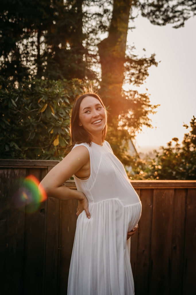 Outdoor sun flare golden hour maternity photo and pose idea and inspo in San Francisco Bay Area for a mother in a white maternity peasant dress that shows off her growing baby bump and looks stunning on her. Captured by San Francisco Bay Area photographer, Xilo Photography
