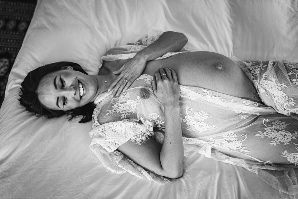 Laying Down Boudoir Maternity Poses For Pregnant Mother: Intimate White Lace Robe Pregnancy photos featuring her baby bump during an at home maternity session for a mother to be in her third trimester in San Francisco Bay Area by Xilo Photography, Inclusive Intimate Photographer