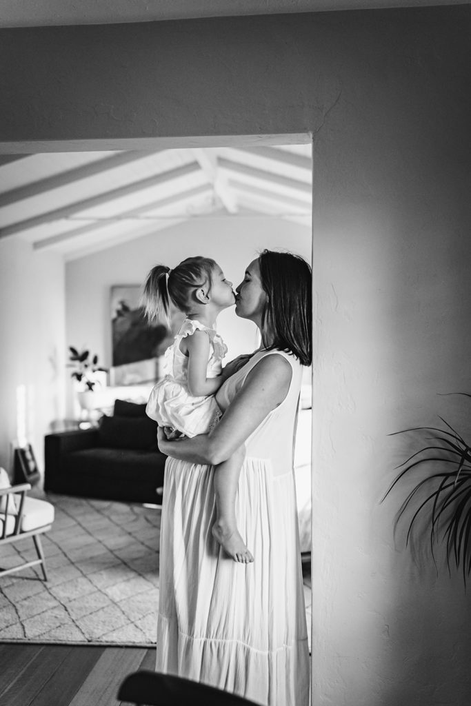 San Francisco Bay Area Family Photographer Xilo Photographer captured this gorgeous photo of mother and young toddler daughter snuggling in maternity photoshoot at home leaning against a wall in their mommy and me matching white dresses
