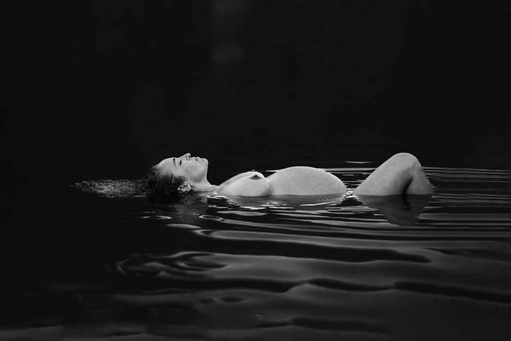Black and white dynamic light maternity photoshoot with a pregnant mama laying down in the Russian River and showcasing her beautiful baby bump and the joy of motherhood. This was captured by SF Bay Area photographer, Kati Douglas of Xilo Photography