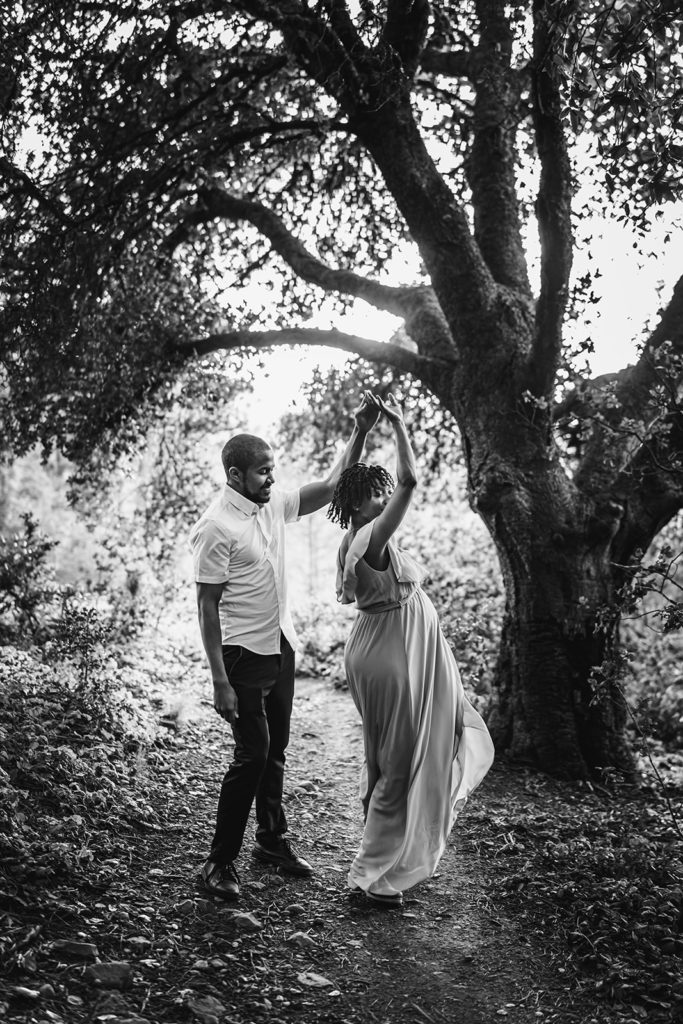 Unique black and white outdoor baby bump photo of husband and wife dancing under the trees in Sea View Trail in San Francisco Bay Area