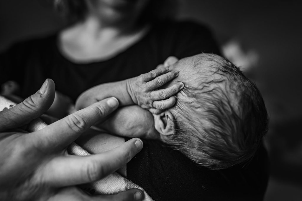 Alta Bates Hospital Newborn baby portrait in parent's arms and snuggling with skin on skin with baby's tiny hands - Perfect example of macro portrait photography with Documentary Photographer, Xilo Photography in San Francisco Bay Area