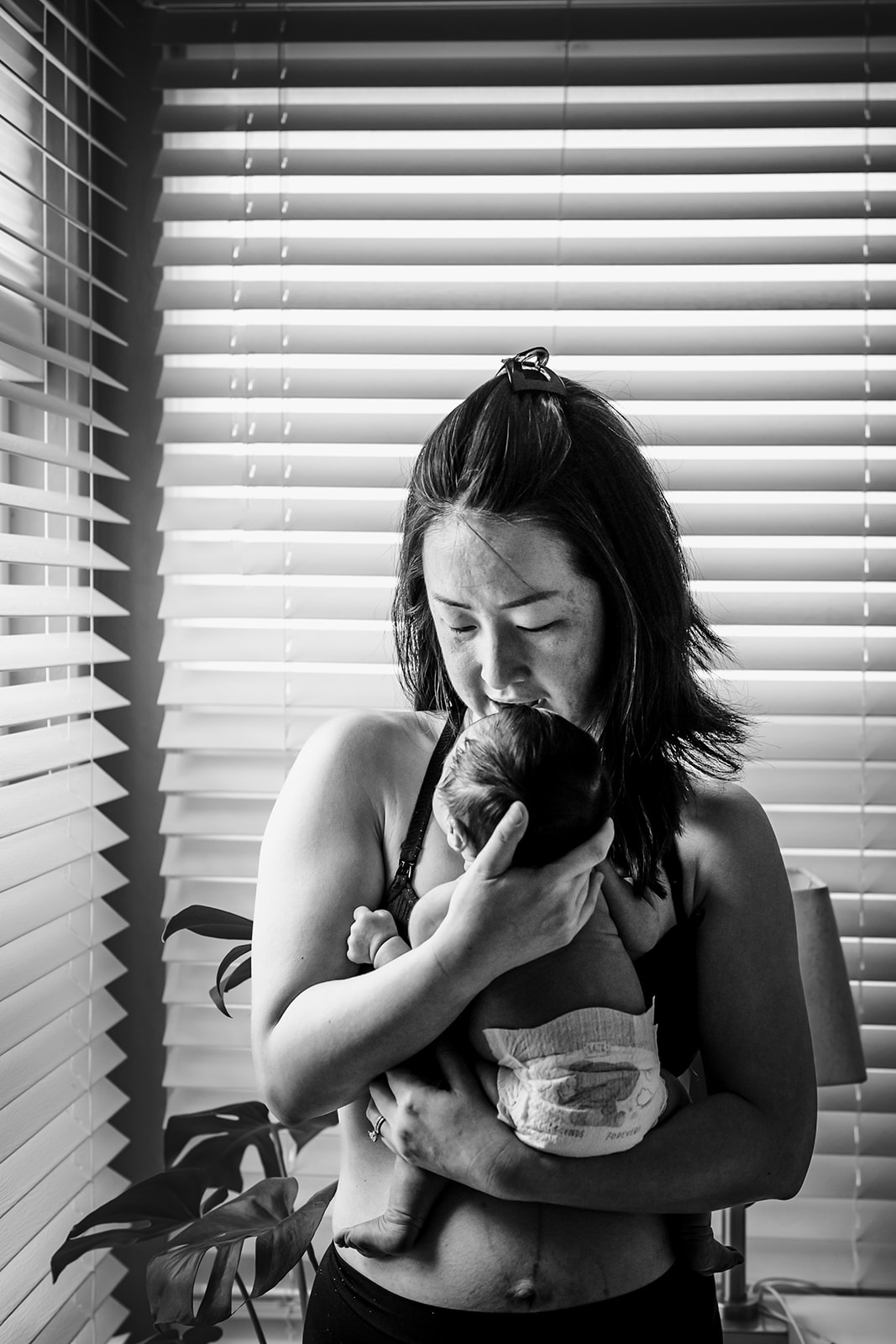 Young mom in her fourth trimester as she snuggles with her newborn baby and has skin to skin time together in Concord, CA photographed by Xilo Photography