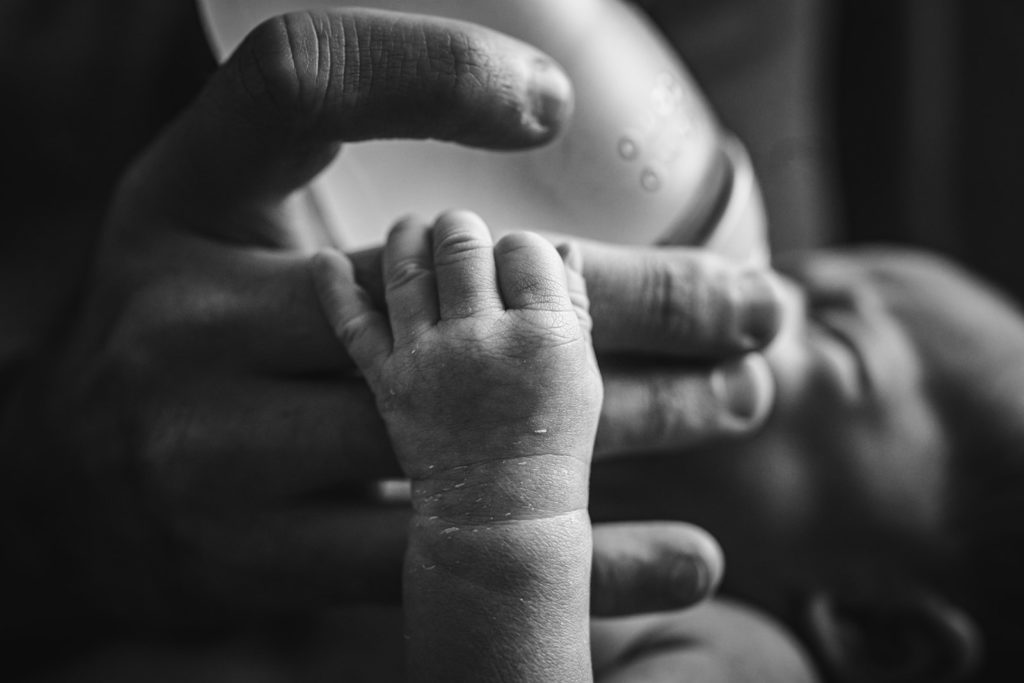 Father and newborn son bonding while newborn grabs onto his father's finger during their at home lifestyle and documentary newborn photography session in El Cerrito, CA by Kati Douglas, Documentary Photographer at Xilo Photography