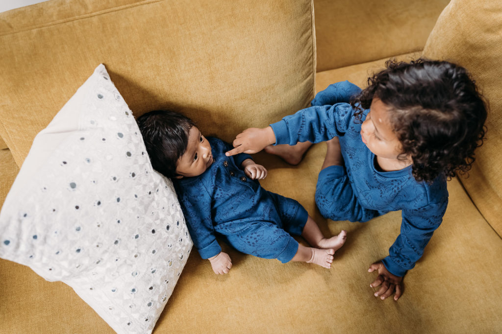 Oakland California newborn photography session with a family of four allowed me to capture this beautiful pose of a toddler and newborn brother in matching outfits spending time together on the couch in their home with an eagle-eye overhead photography angle