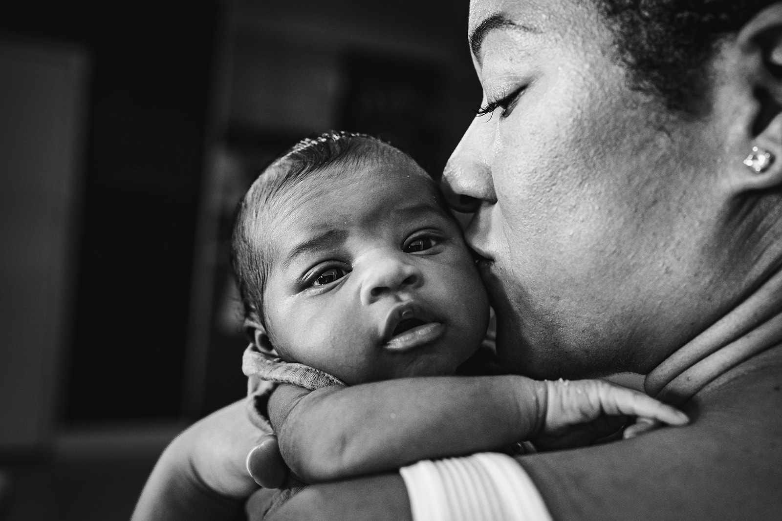 This sweet lifestyle newborn session with a documentary style spin was so incredibly beautiful. This up close portrait of a newborn looking over their mother's shoulder as the mother leans in to kiss her. From Xilo Photography, San Francisco Bay Area Documentary Photographer.